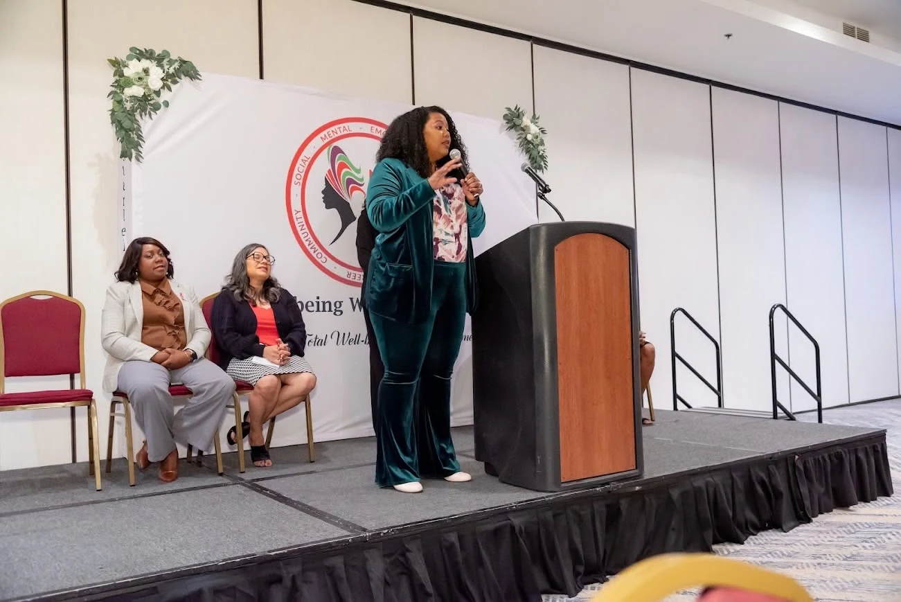 Irene Wilkins speaking on stage in a green suit with seated panelists